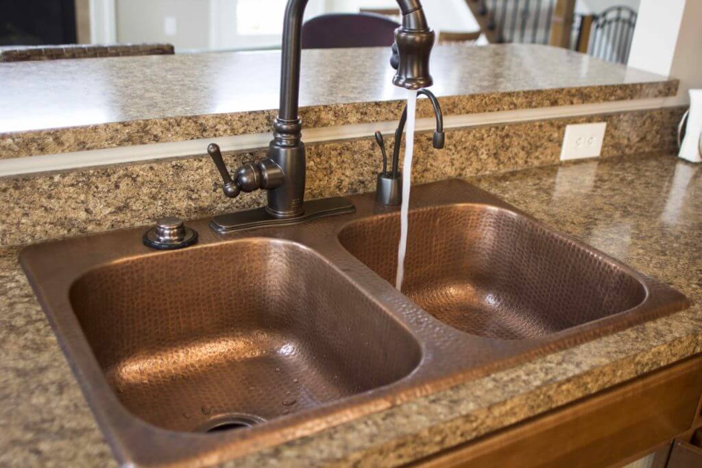 A kitchen with a double-basin hammered copper sink and a bronze faucet, set in a brown granite countertop.