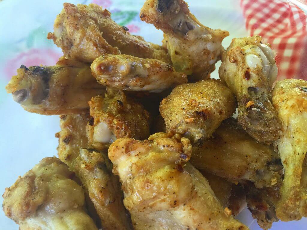 A bowl filled with golden-brown, cooked chicken wings is placed on a table, accompanied by a red and white checkered cloth in the background.