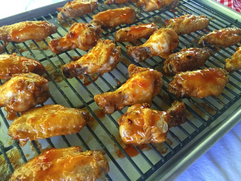 A baking tray with a wire rack holds rows of cooked chicken wings coated in a sticky red sauce.