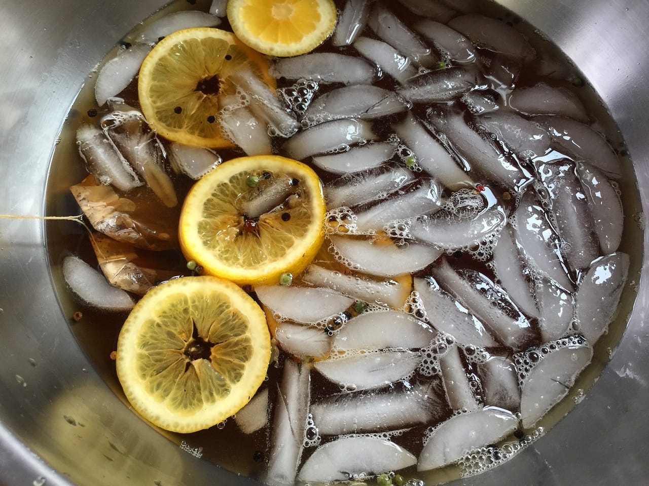 a sweet tea brine with salt, pepper & a lemon in a bowl of ice