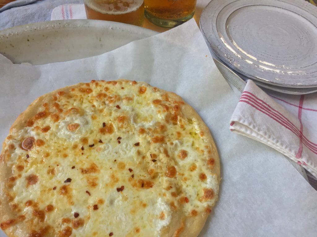 A cheese pizza on a tray with two glasses of beer and a stack of plates on a table with a red and white napkin.