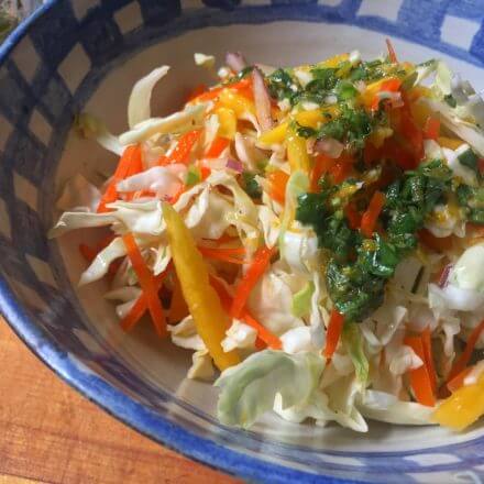 A bowl of fresh coleslaw made with shredded cabbage, carrots, bell peppers, onions, and mango, mixed together and ready to serve.
