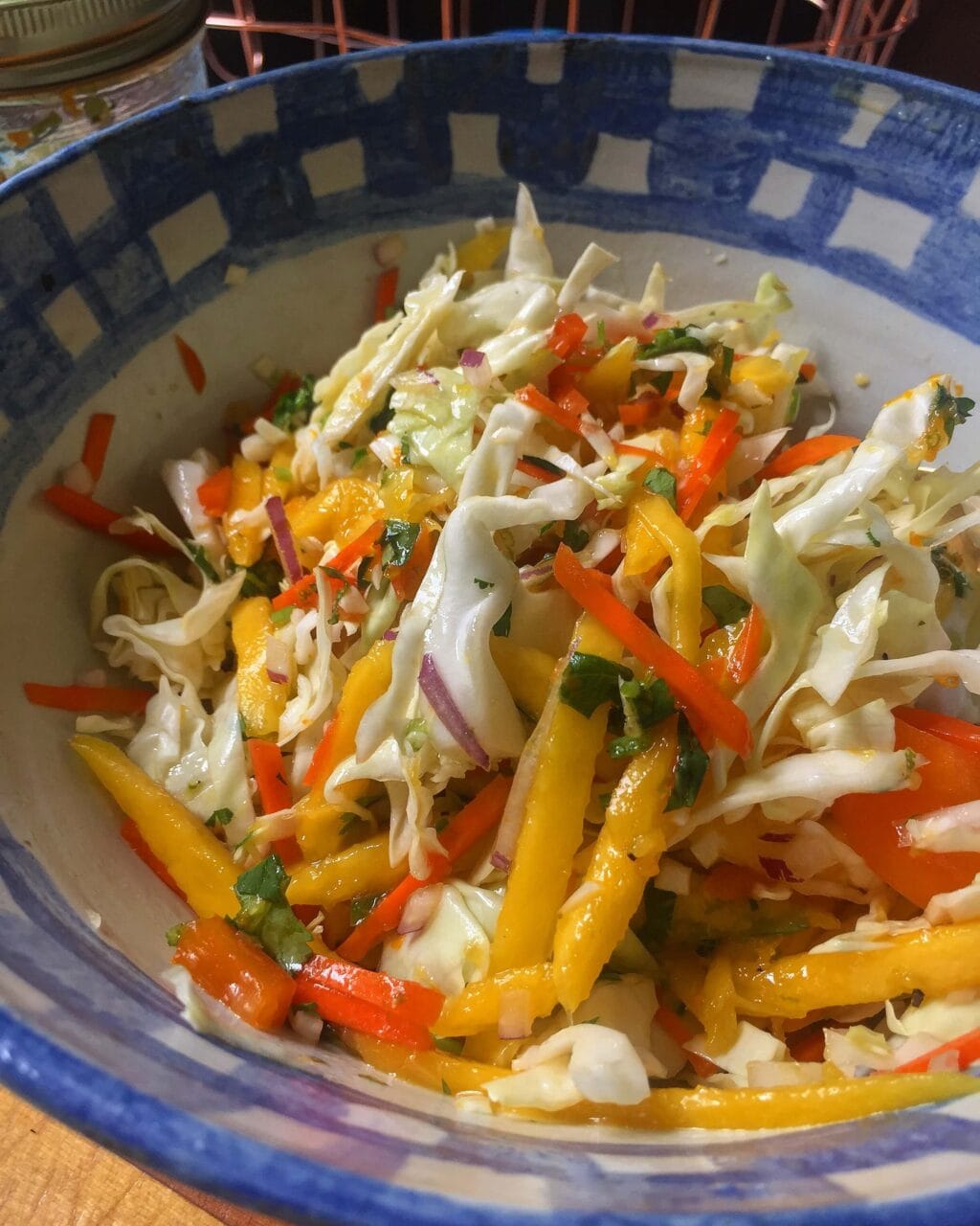 A bowl of fresh coleslaw made with shredded cabbage, carrots, bell peppers, onions, and mango, mixed together and ready to serve.