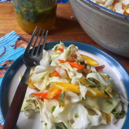 A bowl of fresh coleslaw made with shredded cabbage, carrots, bell peppers, onions, and mango, mixed together and ready to serve.