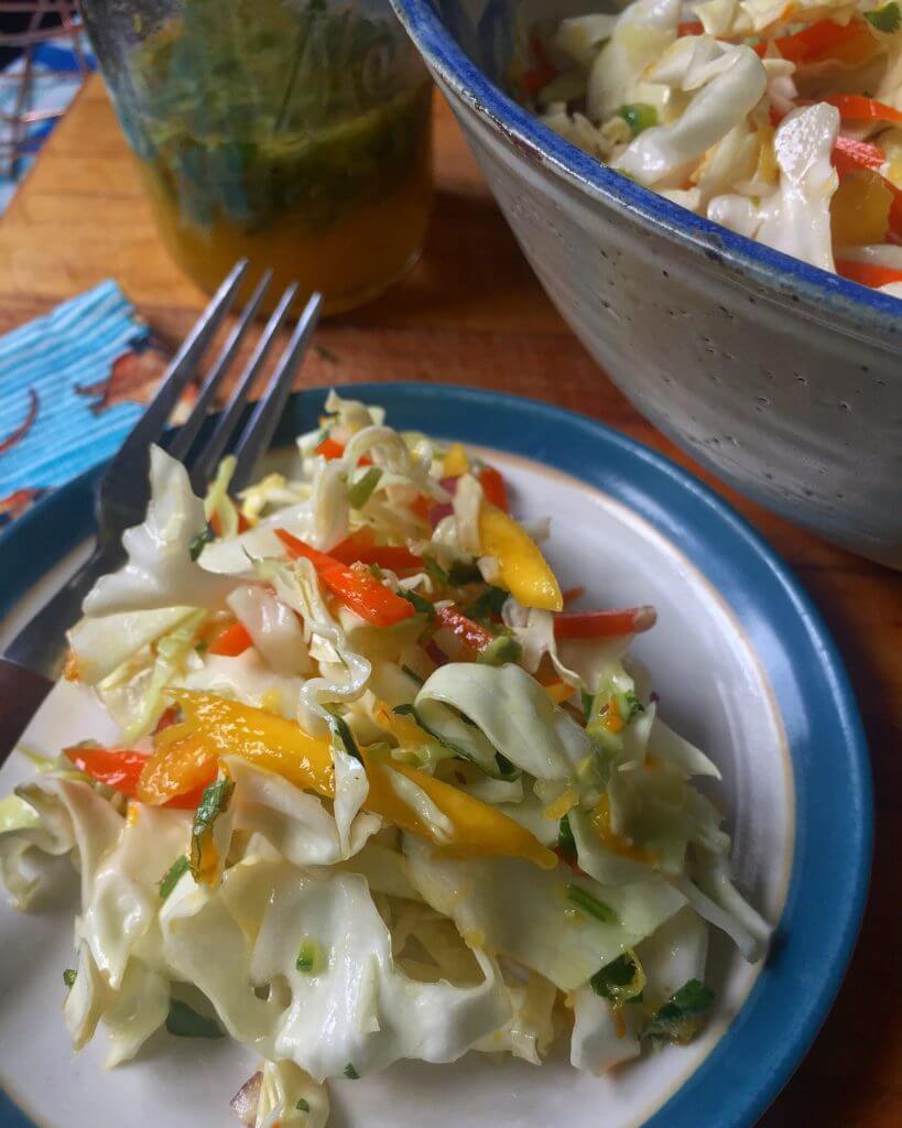 A bowl of fresh coleslaw made with shredded cabbage, carrots, bell peppers, onions, and mango, mixed together and ready to serve.