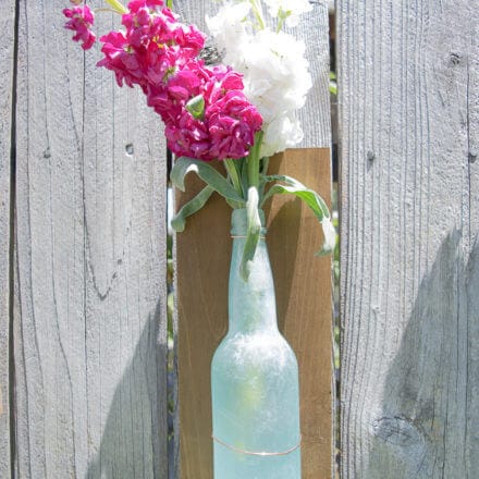 a diy bottle vase attached to a piece of wood by a copper wire