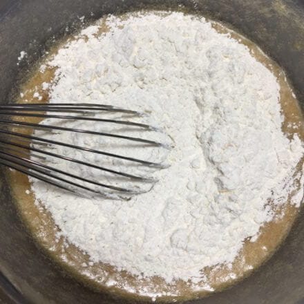 A mixing bowl with batter and flour being combined with a whisk.