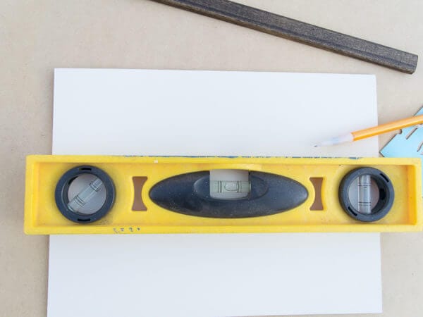A yellow level tool placed on a white surface, with a pencil, ruler, and a wooden strip nearby.