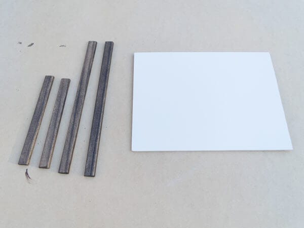 Four wooden strips of varying lengths are laid out next to a rectangular white board on a plain surface.