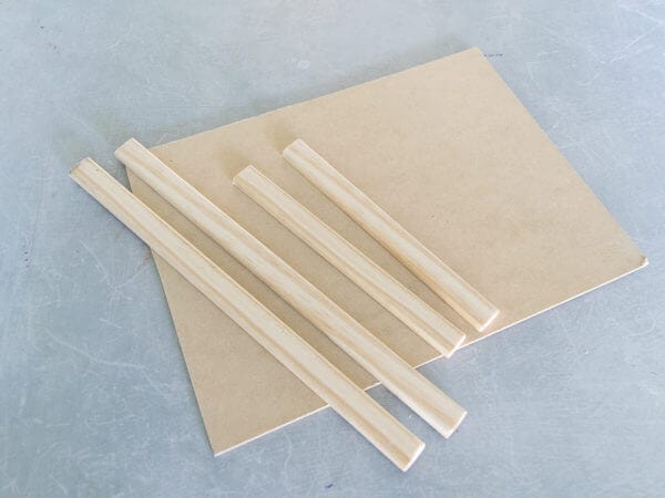 Four light wooden strips are laid out on top of a rectangular wooden board on a gray surface.