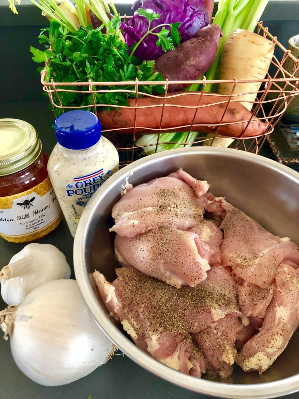 Ingredients for honey mustard sheet pan chicken: raw seasoned chicken, honey, mustard, garlic, and assorted fresh vegetables.