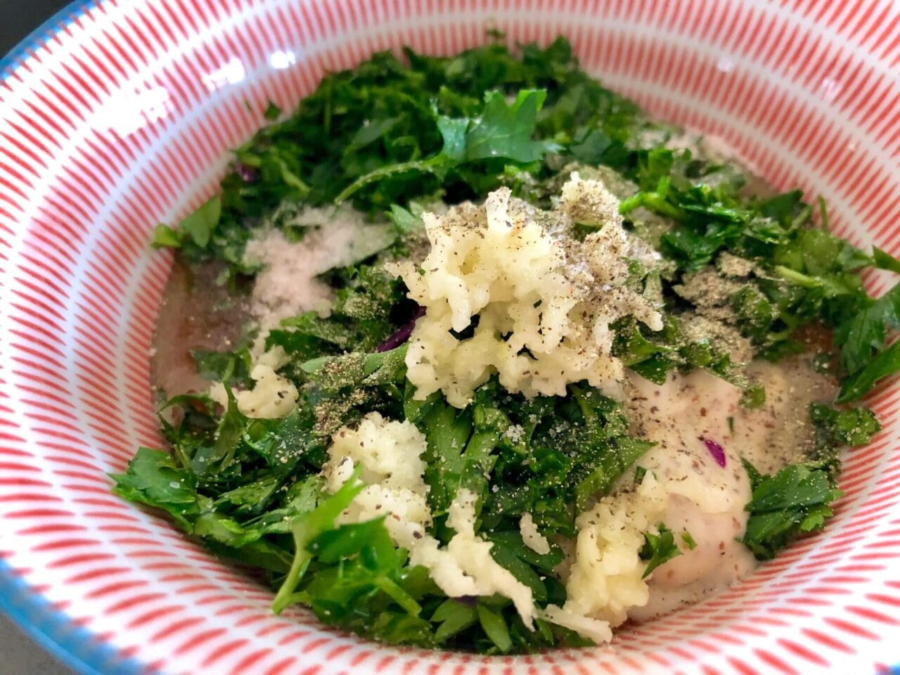 A bowl with a mixture of chopped fresh herbs, minced garlic, and seasoning.