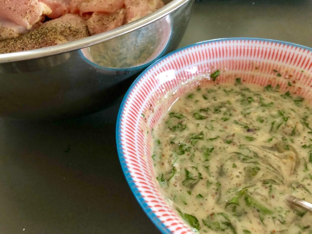A bowl of seasoned raw chicken next to a bowl of freshly mixed honey mustard sauce with herbs.