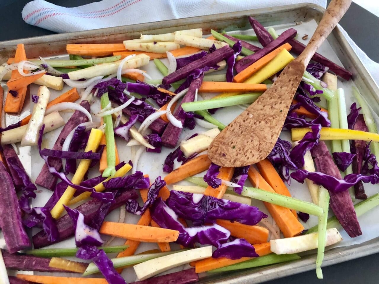 A sheet pan with an assortment of seasoned root vegetables and onions, ready for roasting.