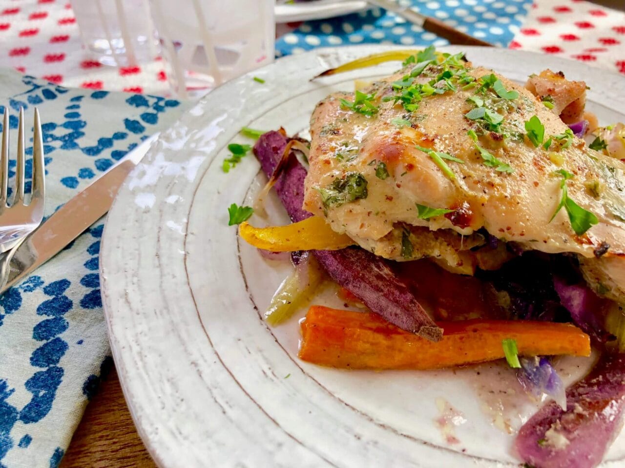 A plated serving of roasted honey mustard chicken with assorted root vegetables, garnished with fresh herbs.