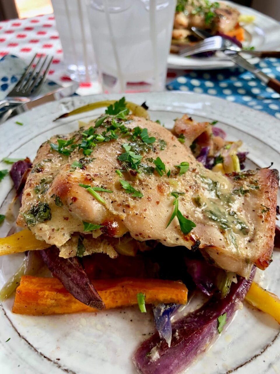 A plate of roasted honey mustard chicken with root vegetables, garnished with fresh herbs, set on a colorful table setting.