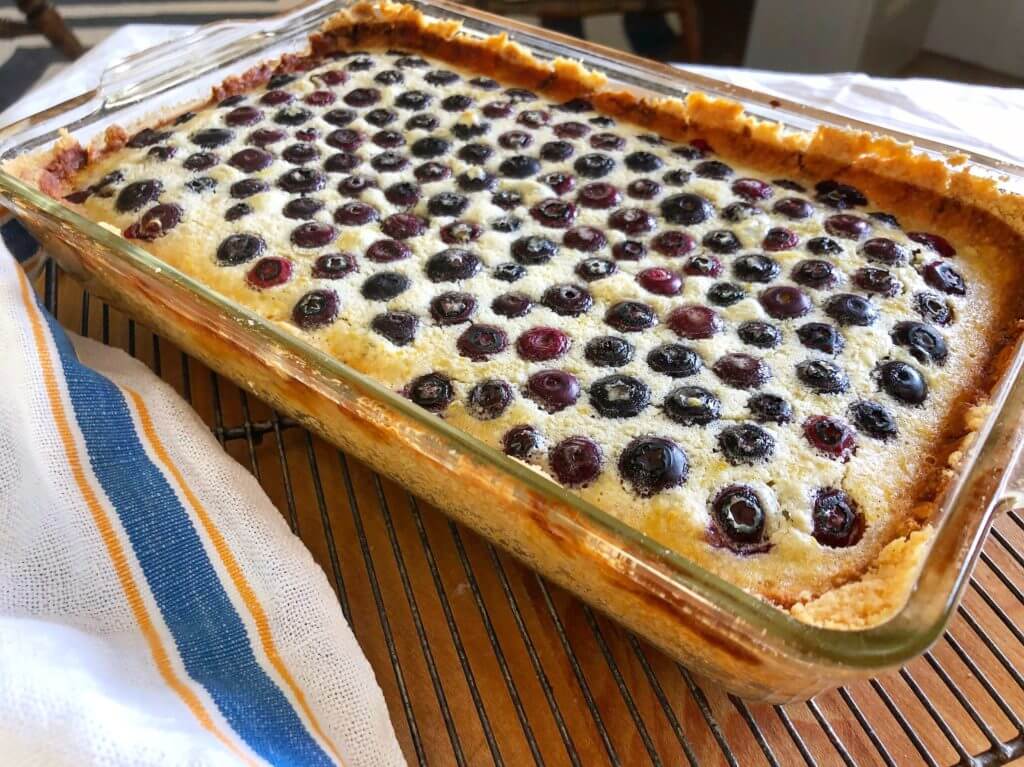 A freshly baked lemon blueberry dessert in a glass dish, cooling on a wire rack.