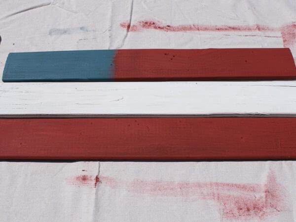Three wooden planks are painted in blue, white, and red, with one plank showing a blend of blue and red.