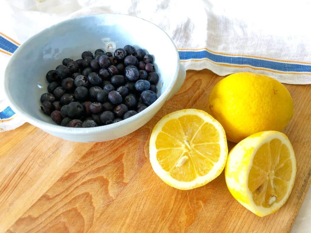 A bowl of blueberries and two halved lemons on a wooden board.