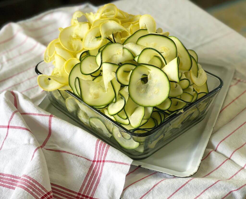 A glass dish filled with sliced zucchini and yellow squash on a cloth.