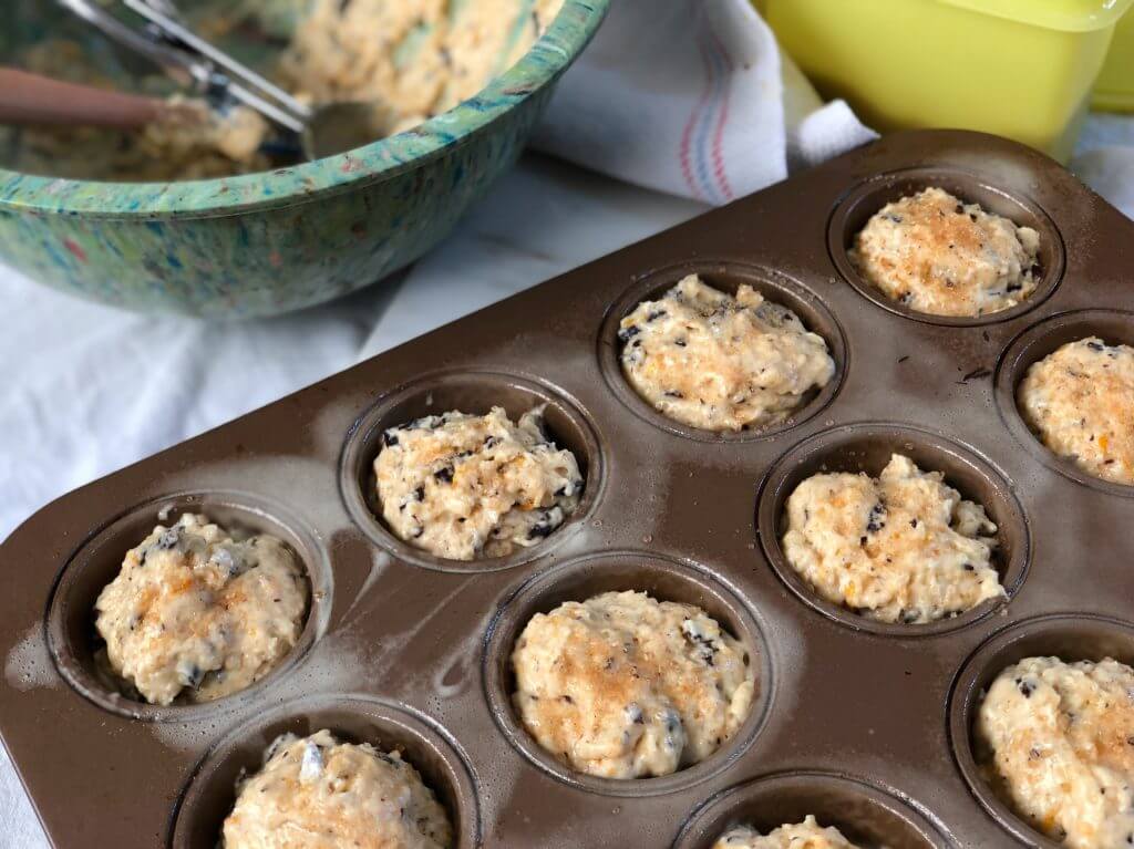 A muffin tray filled with unbaked muffin batter beside a mixing bowl.