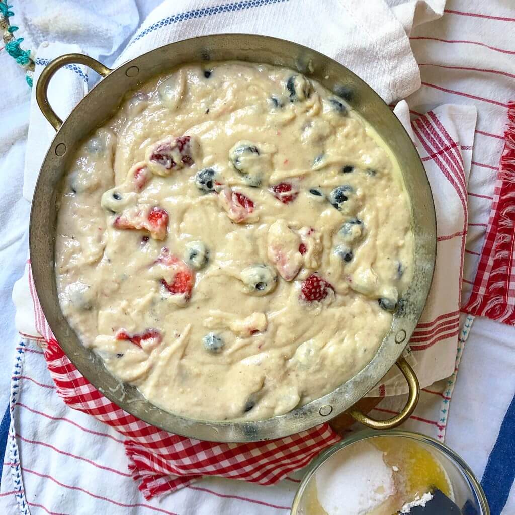 A baking dish filled with mixed berry batter rests on a red and white checkered cloth.