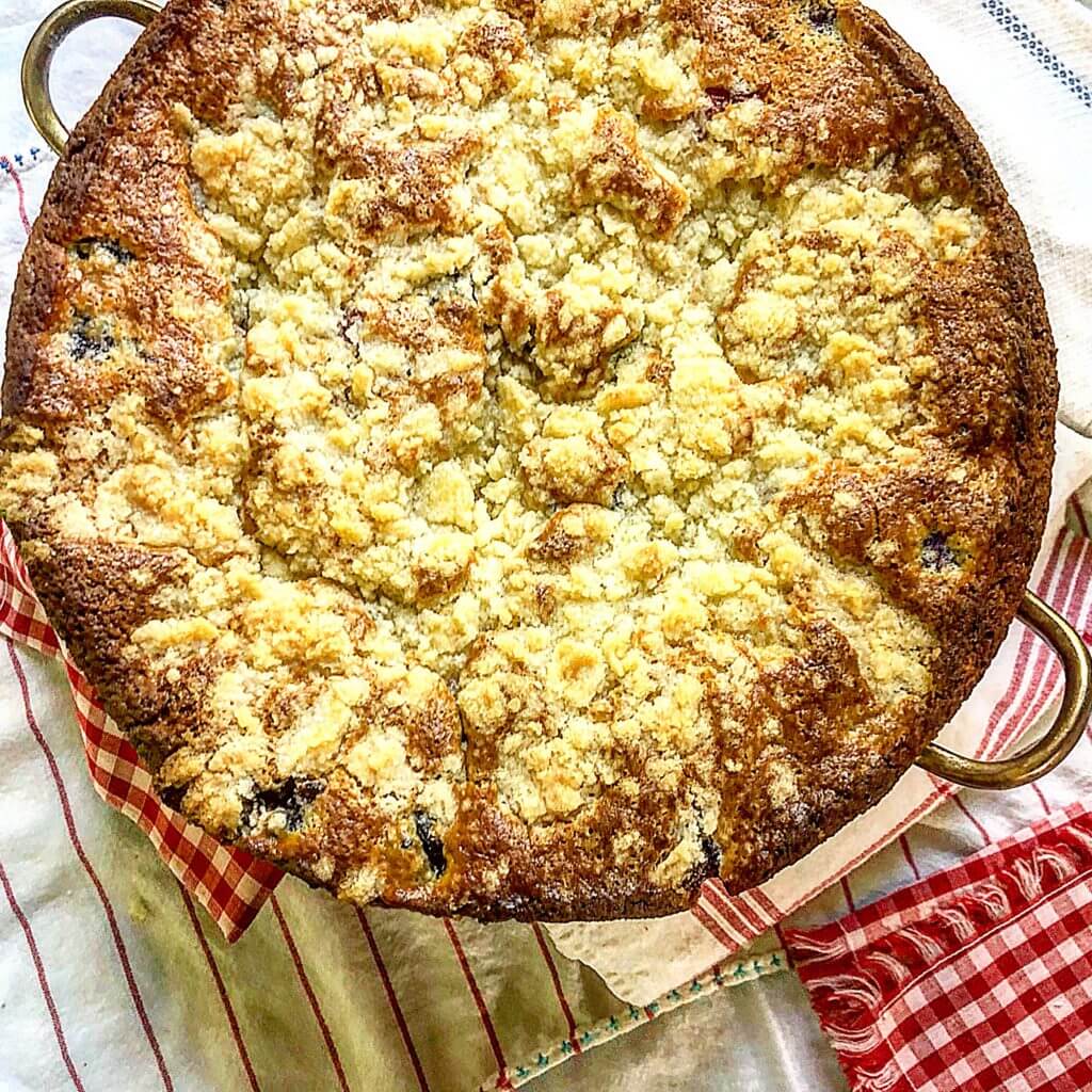 A freshly baked mixed berry crumble cake in a baking dish sits on a red and white checkered cloth.