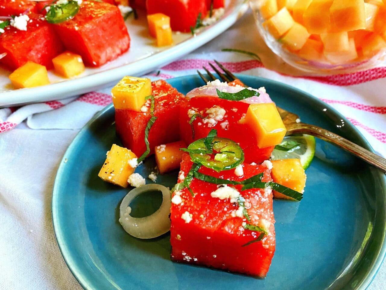 Plate of watermelon and cheese cubes garnished with herbs and jalapeno slices.