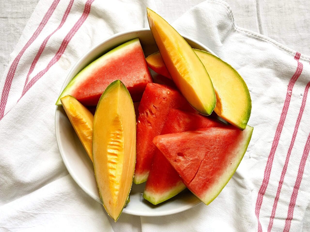 Plate of sliced watermelon and cantaloupe on a white cloth with red stripes.