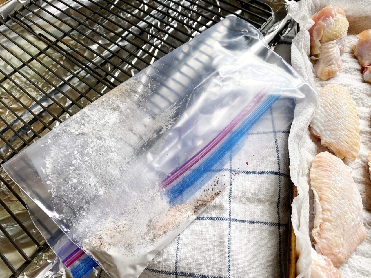 Empty plastic bag with flour residue next to raw chicken wings on paper towels.