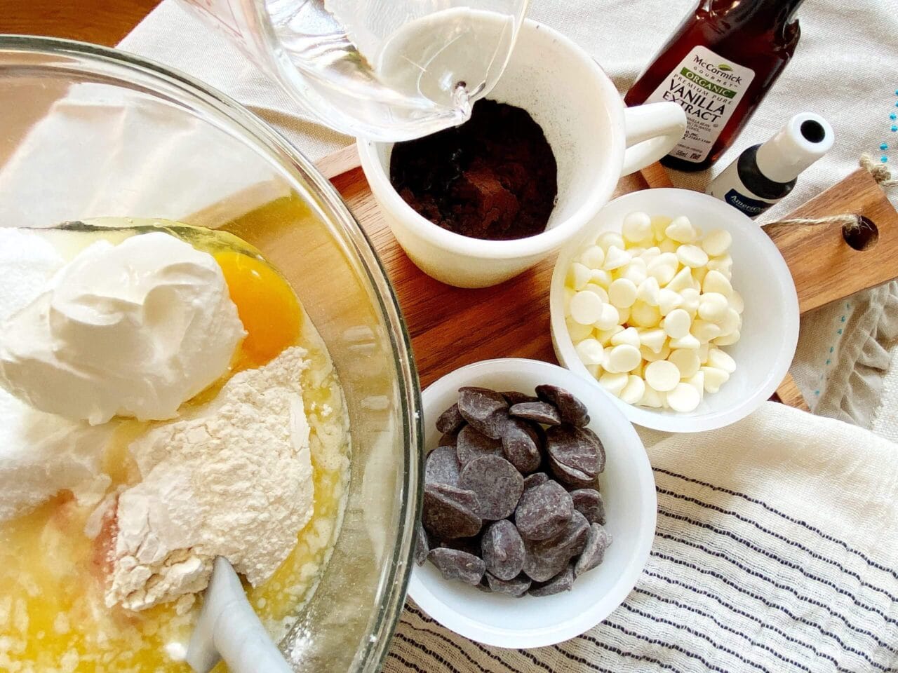 A top-down view of baking ingredients, including flour, sour cream, eggs, vanilla extract, cocoa powder, and chocolate chips, ready to be mixed.