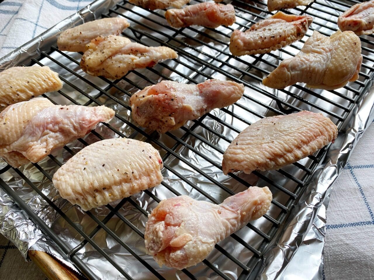 Raw, seasoned chicken wings arranged on a wire rack over a foil-lined baking sheet, ready to be cooked.