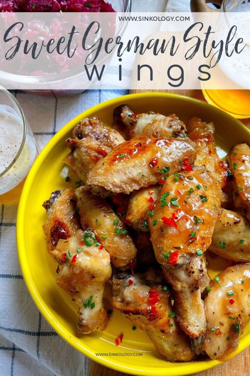 A bowl of glazed chicken wings garnished with chopped herbs and red chilies, with the text "Sweet German Style Wings" overlaying the image. In the background are a bowl of pickled red cabbage and a glass of beer.