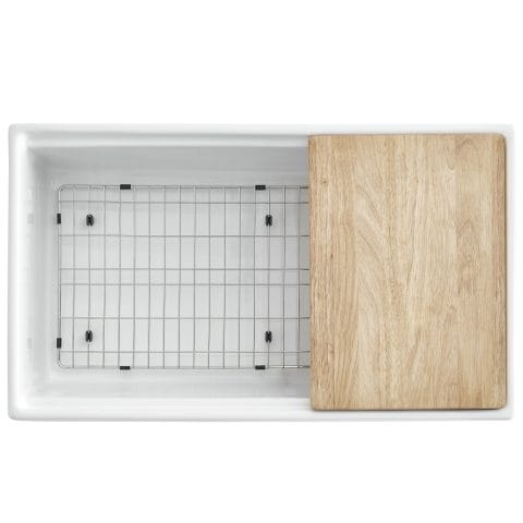 A white fireclay farmhouse workstation kitchen sink with wooden cutting board and stainless steel bottom grid.
