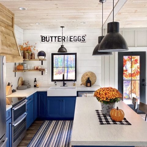 A glossy white rectangular Quick-Fit® drop-in farmhouse sink in the center of a bohemian designed kitchen with blue cabinets and white shiplap walls.