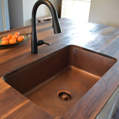 A kitchen with a copper undermount sink, bronze faucet, natural wood countertop.