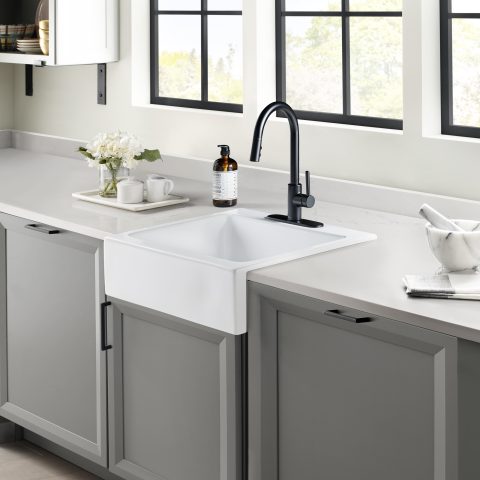 A glossy white rectangular Quick-Fit® drop-in farmhouse sink made in fireclay with a modern black faucet set in solid surface gray countertop and dark gray cabinets.