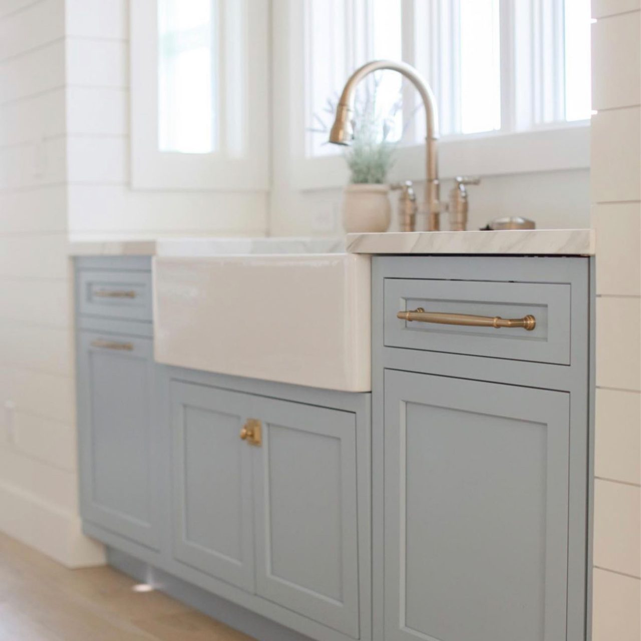 A glossy white rectangular double bowl undermount farmhouse sink in baby blue cabinets with a stainless steel faucet and large windows over sink.