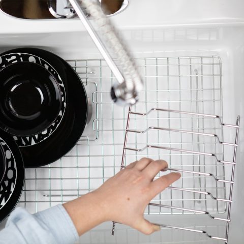 Single sink basin made of white fireclay full of dishes with man placing stainless steel organizing GridLogic bottom grid.