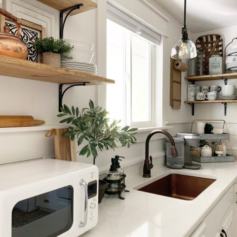 A kitchen with a copper undermount sink, bronze faucet, white countertop and cabinets.