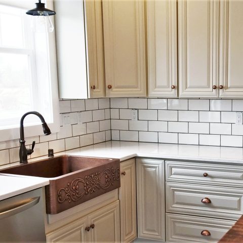 A copper rectangular undermount farmhouse sink in a white kitchen