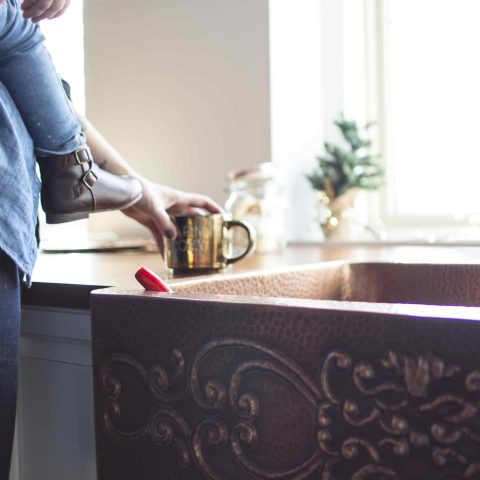 A mother sitting a coffee cup next to a copper rectangular undermount farmhouse sink.