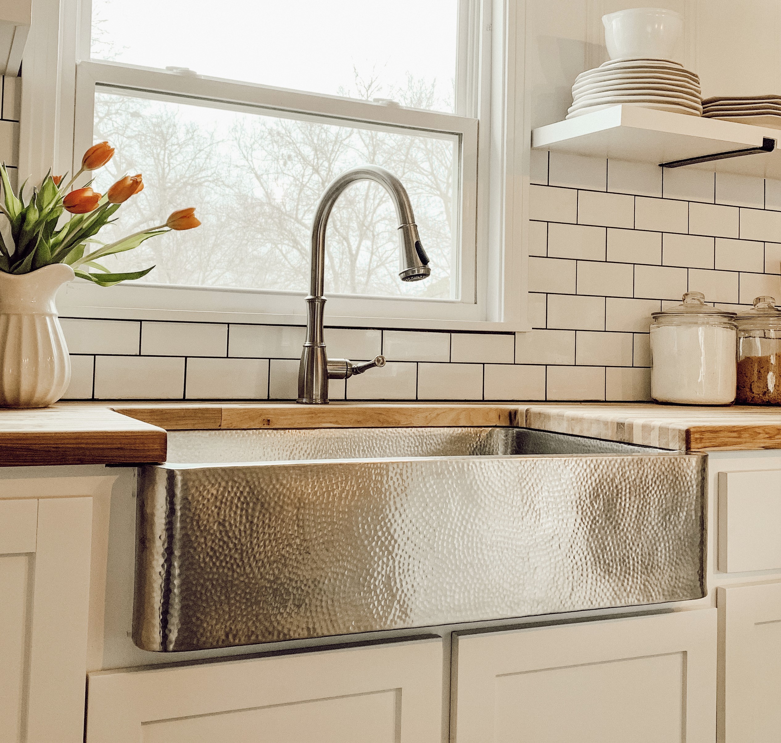 A hand hammered brushed stainless steel rectangular undermount farmhouse sink in a home kitchen.