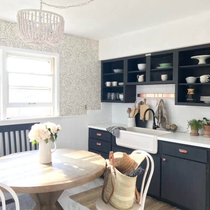 Bright kitchen with a round wooden dining table, black open cabinets, white countertops, and a farmhouse sink.