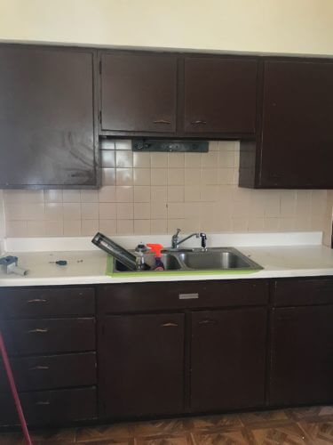 Dark brown kitchen cabinets with a stainless steel sink and light beige tiled backsplash.