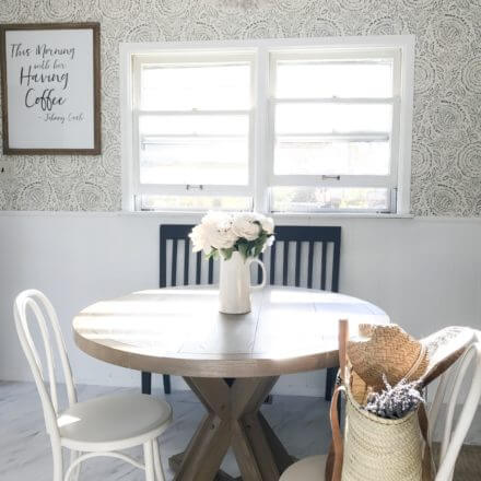 Cozy dining area with a round wooden table, white and black chairs, and a vase of flowers.