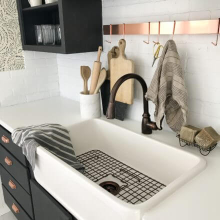 Farmhouse kitchen sink with a bronze faucet, black cabinets, and various kitchen utensils and towels on the counter.