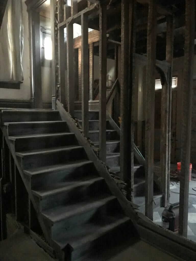 A dark, unfinished staircase with exposed wooden framing and a partially gutted wall in a house under renovation.