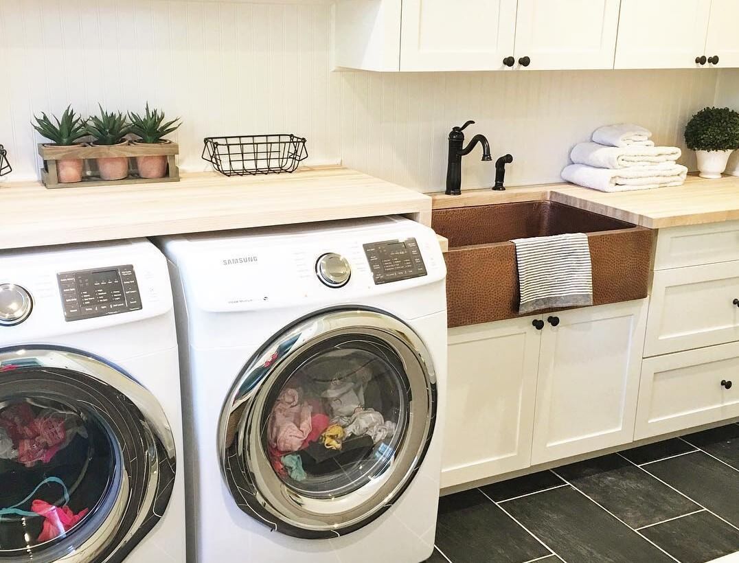 A modern laundry room with white front-loading washer and dryer, and a copper sink.