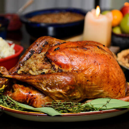 Roasted turkey with stuffing on a platter, surrounded by side dishes and a lit candle in the background.